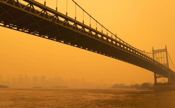 A hazy New York, New York, skyline & bridge colored by orange wildfire smoke