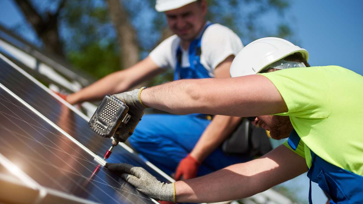 Deux installateurs solaires certifiés en équipement de sécurité fixant des panneaux solaires sur des râteliers de montage sur un toit résidentiel.