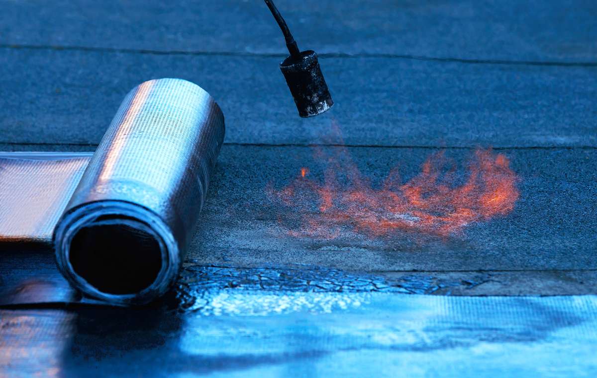 A roofer using a hot air gun to heat-weld the seam on a white TPO flat roof membrane.