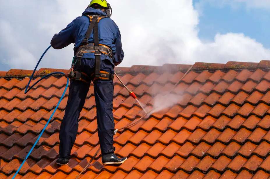 Un professionnel avec un harnais de sécurité utilisant un nettoyeur haute pression pour nettoyer un toit en tuiles en toute sécurité.
