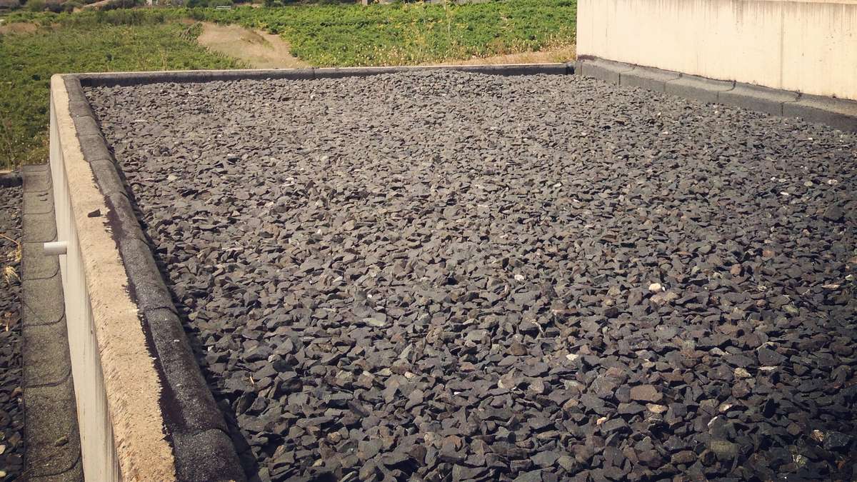 A flat roof covered in a layer of smooth gray gravel, with a few leaves scattered on top.