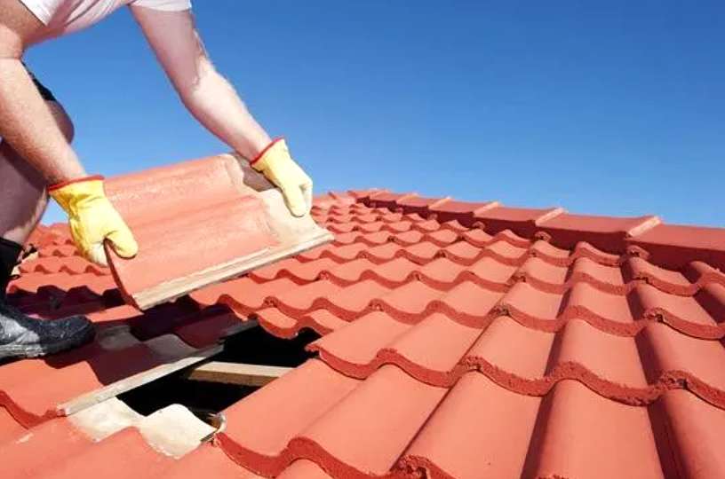 Un couvreur glissant soigneusement une nouvelle tuile en béton en place pour remplacer une tuile cassée.