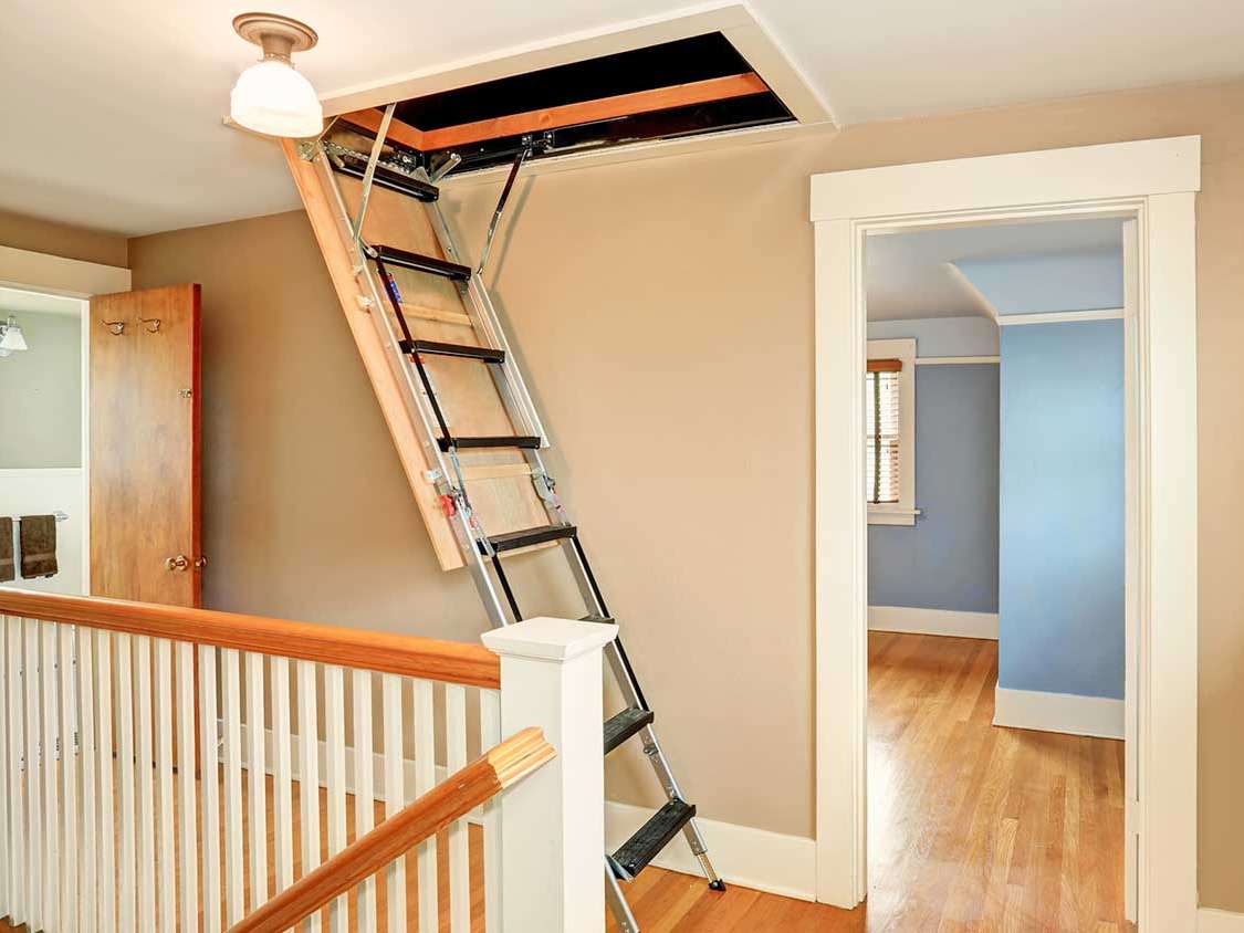 A person pulling down a retractable attic ladder from the ceiling.