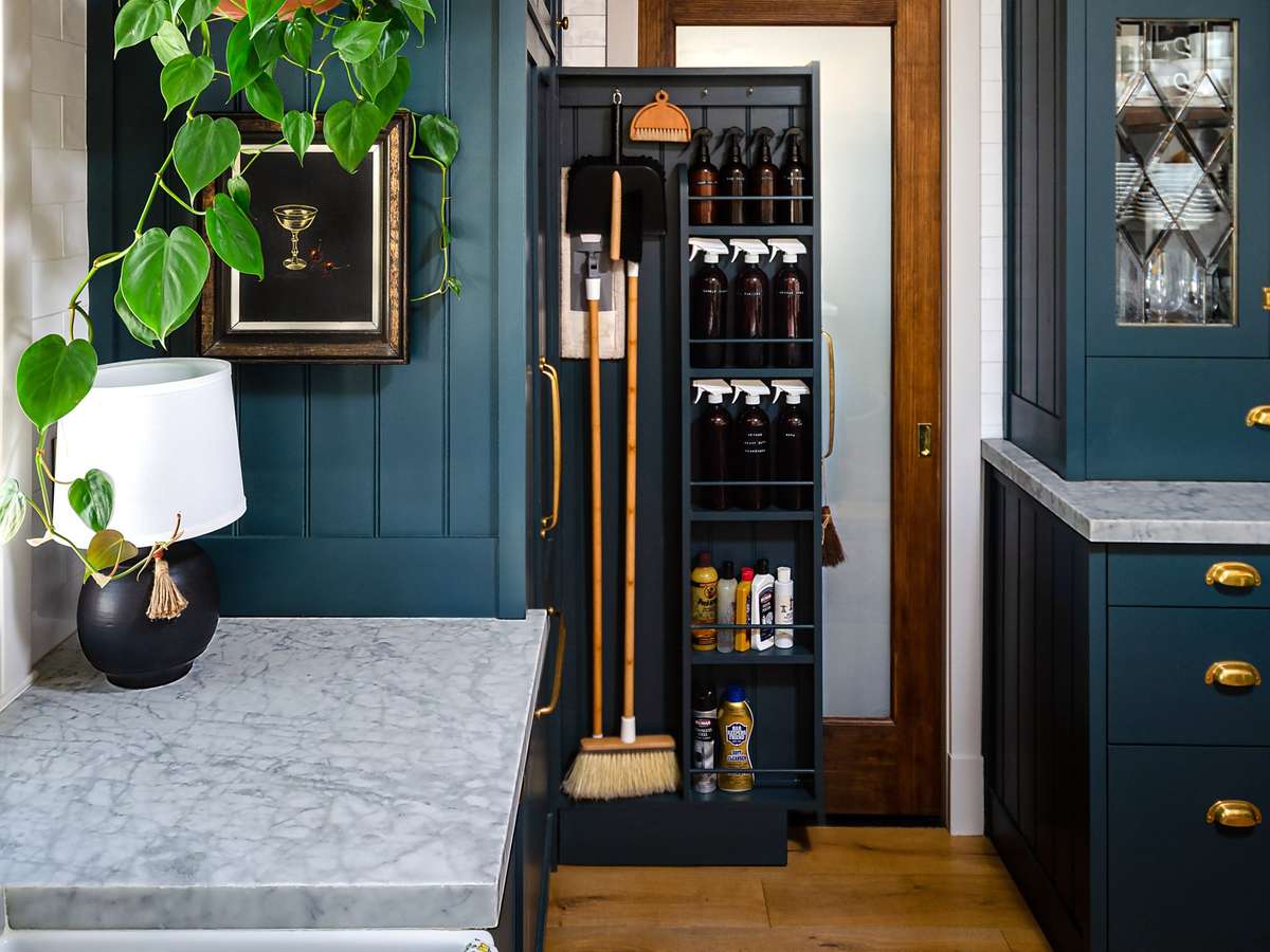 A tall, narrow pull-out cabinet for brooms, mops, and a vacuum beside a refrigerator.