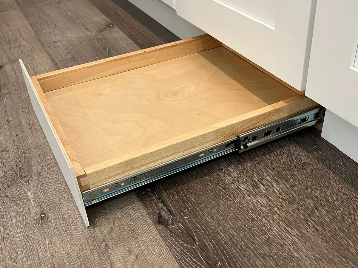 A hidden toe kick drawer is pulled out to show where flat items like baking trays are stored.